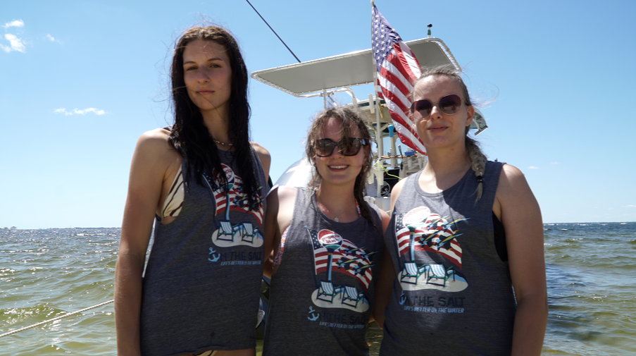 Three women in matching shirts on a boat with the American flag.