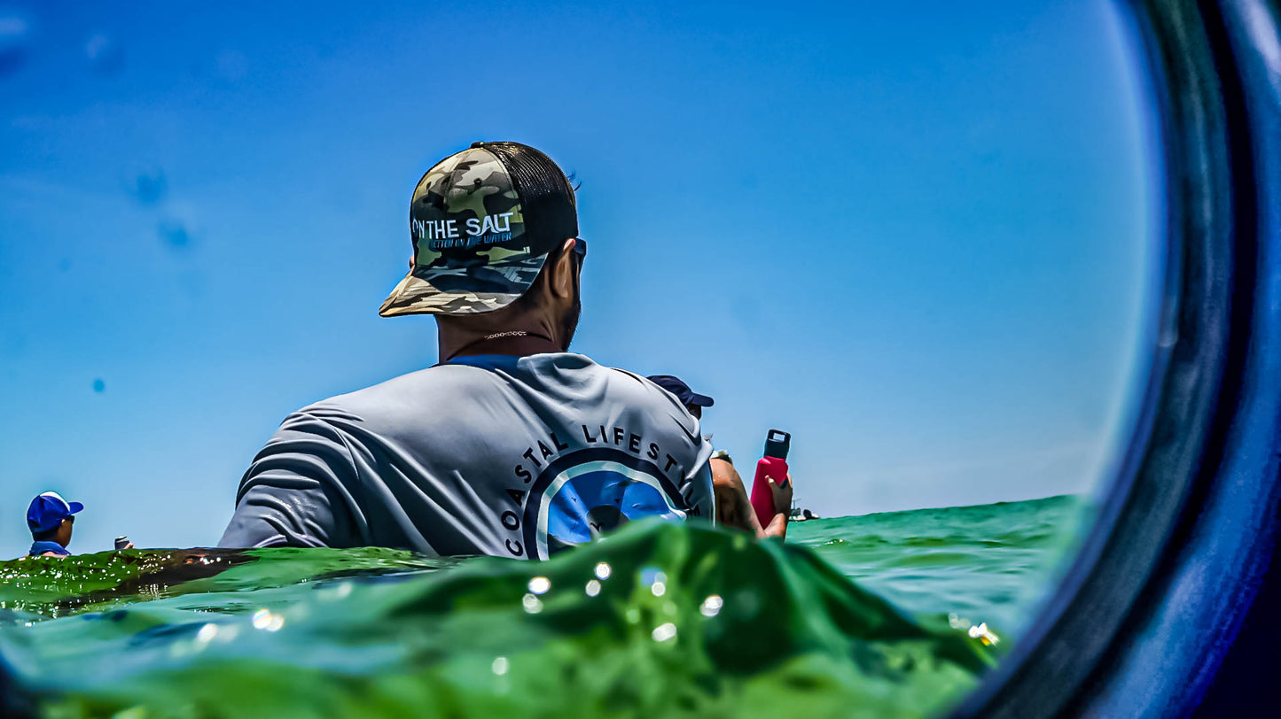 Person in a kayak wearing a cap and shirt with text, looking out over water.