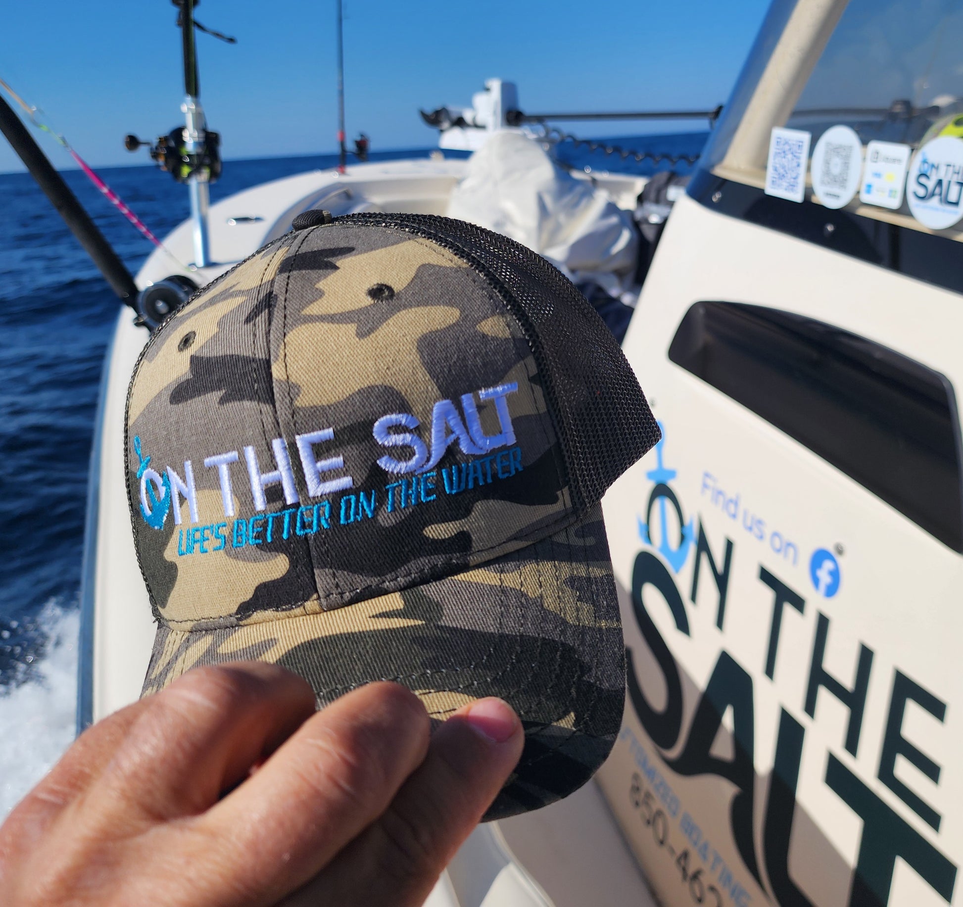 Camouflage cap with 'On the Salt' text held on a boat.
