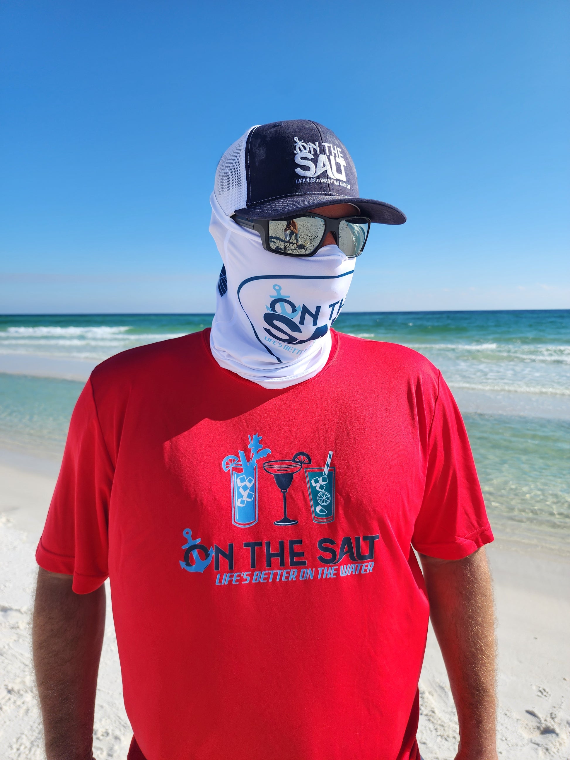 A person wearing a red t-shirt with the text 'ON THE SALT' and a graphic of two glasses, one with a straw for a drink, on the front. The person is also wearing a white sun mask covering the lower half of their face.