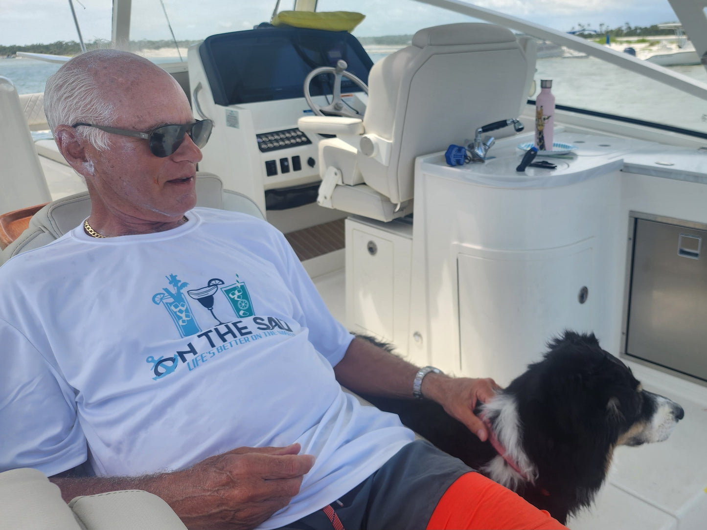 Man sitting on a boat with a dog, wearing a 'On the Sea' t-shirt.