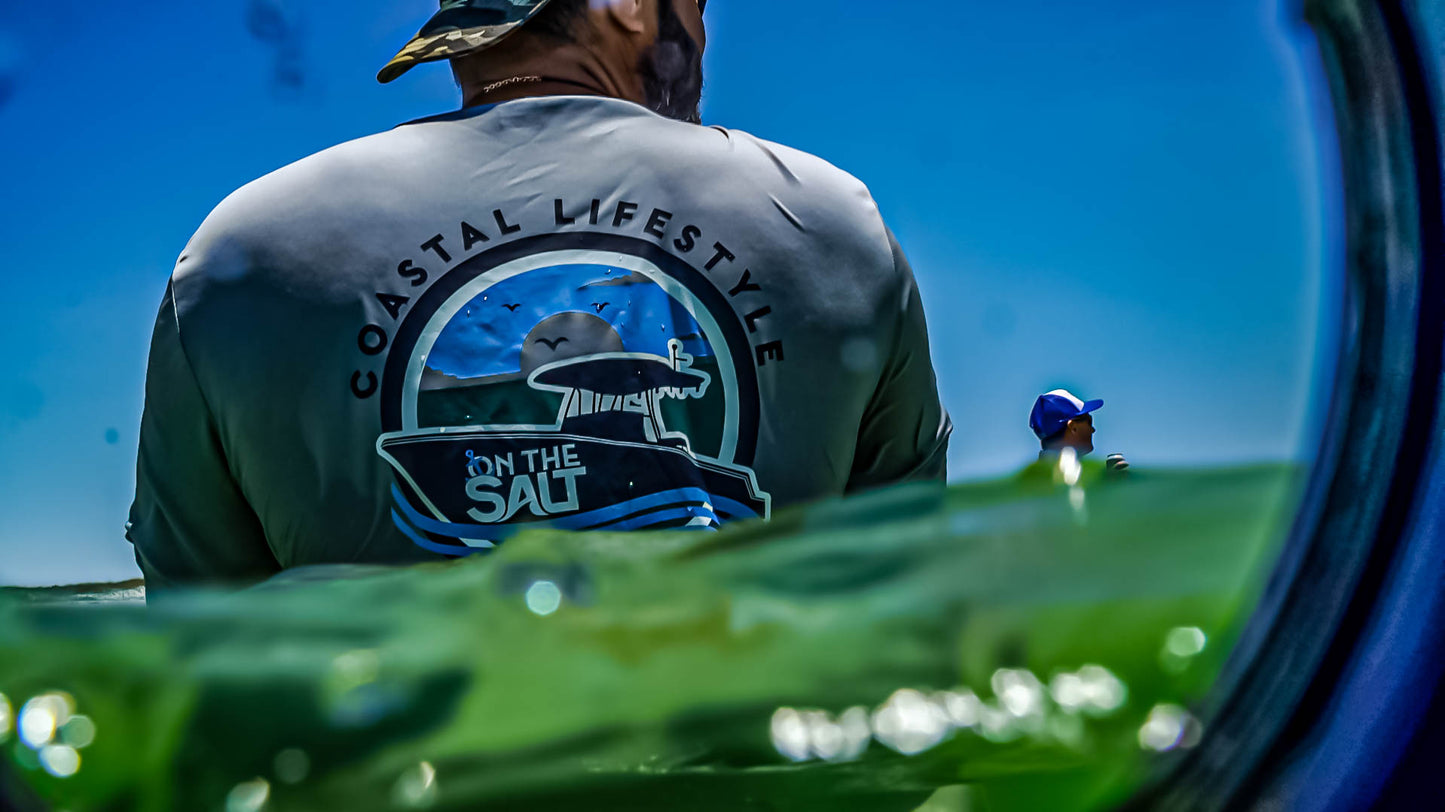 Person wearing a 'Coastal Lifestyle' shirt with a scenic design, sitting on a boat.