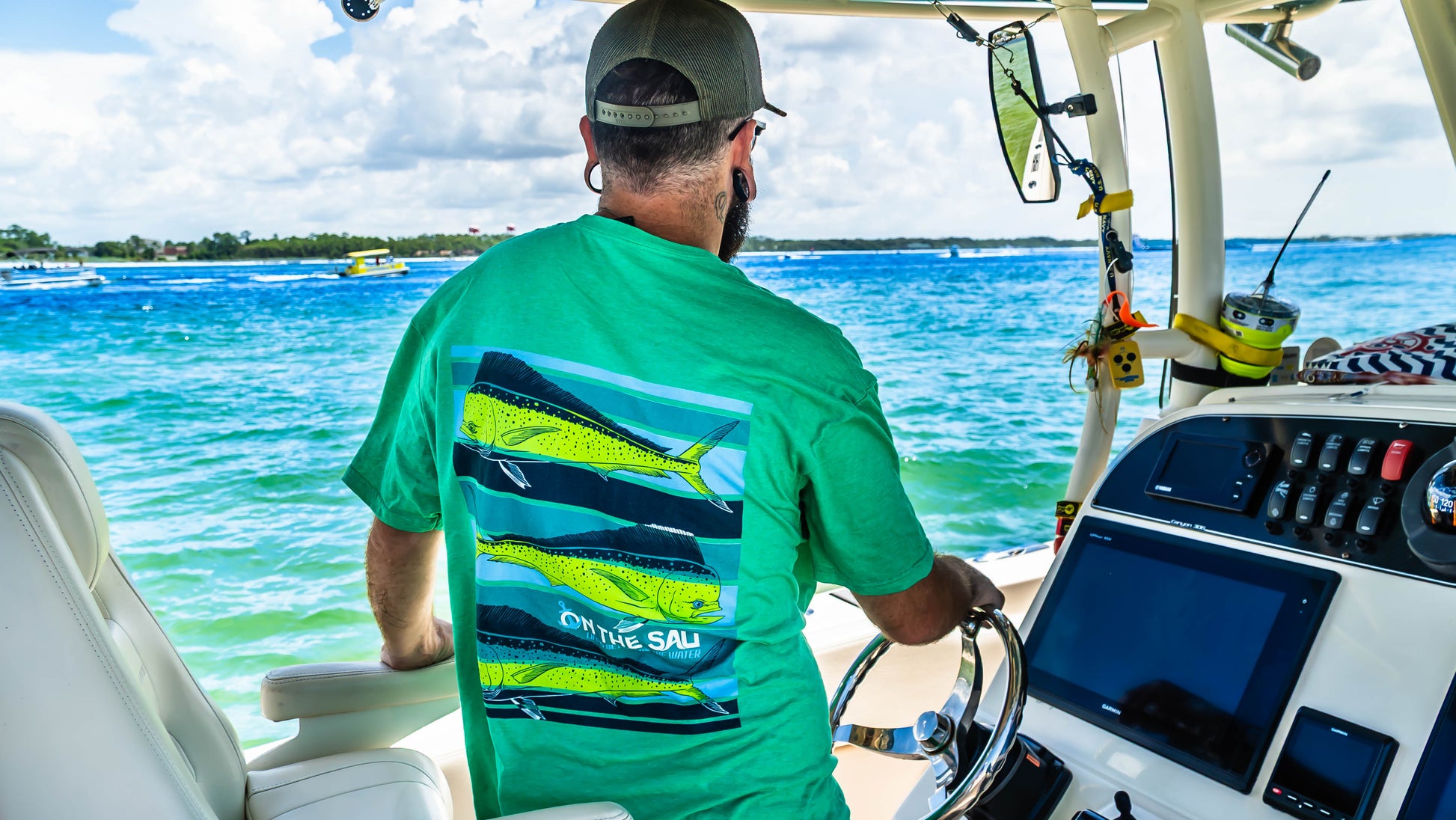 Man on a boat wearing a green shirt with fish design, steering the wheel.