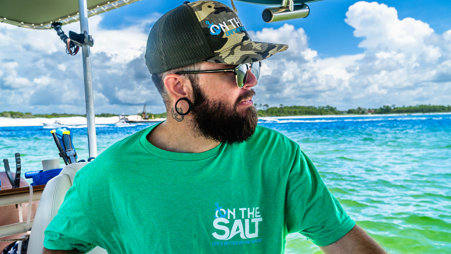 Man wearing a green 'On the Salt' shirt on a boat with a scenic background